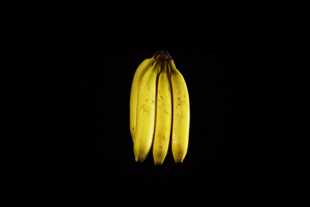 Bunch of yellow ripe bananas with drops of water on black background, copy space.