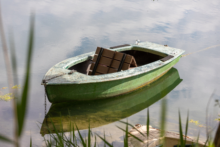 Closeup View of Dinghy Paddle Boat on Clear Water. Oar, rusty Chain and Rope Resting inside the Blue Watercraftの写真素材