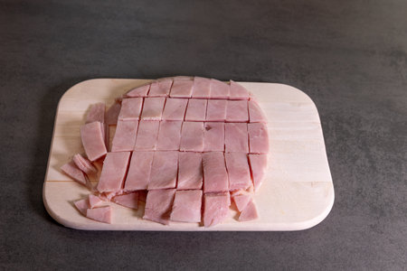 Diced ham neatly arranged on a wooden cutting board, ready for use in cooking or recipes.の写真素材