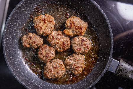 Perfectly seared burger patties in a frying pan, browned and ready to serve, sitting in flavorful...