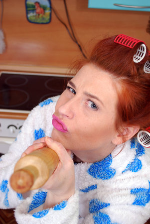 Young housewife in curlers threatening aiming rolling pinの写真素材