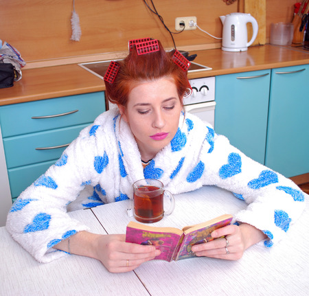 The red-haired girl in a dressing gown in kitchen wound hair curlers, guided black to tea and sat down to read the novelの写真素材