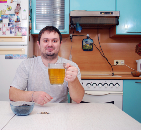 The young man drinks beer in kitchenの写真素材