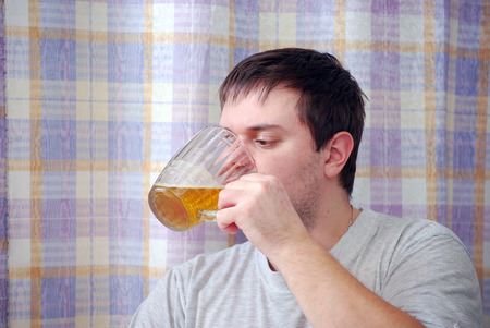 The young man drinks beer in kitchenの写真素材
