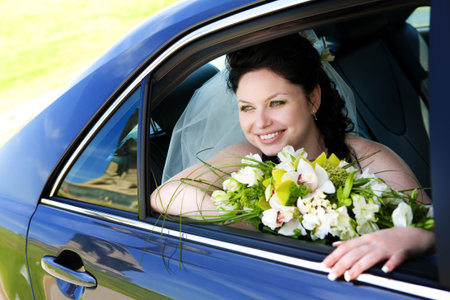 happy bride with flower bouquet siting in the carの写真素材