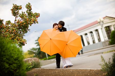 kiss of bride and groom with orange umbrellas の写真素材