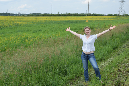 A smiling girl standing on the edge of the field with yellow small flowers.の写真素材