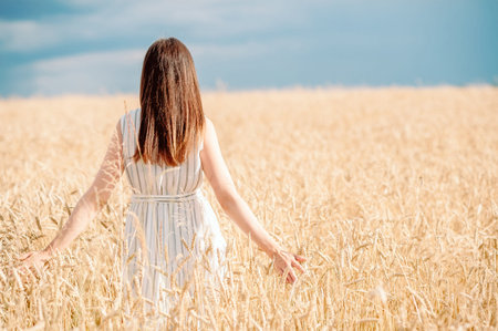 a young girl of about 20 walks across a wheat field with her backs spreading her arms to the sides...