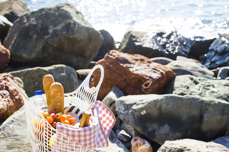 a romantic picnic by the sea - a basket with food and wine, fruit and bread on the coverlet. Background. Copyspaceの写真素材