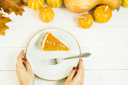 a slice of American pumpkin pie on Thanksgiving Day, decorated with pumpkin seeds in female hands. on a white tableの写真素材