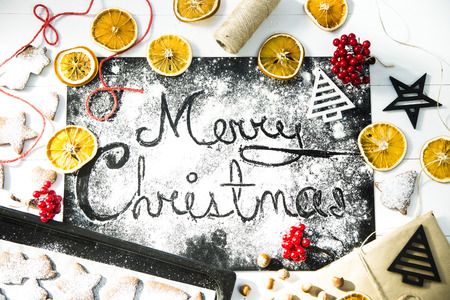 inscription Christmas on a black board sprinkled with flour among the Christmas decor, ginger biscuits and dried orangesの写真素材