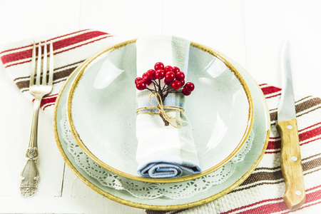 a table setting for Christmas with a viburnum on a plate and an ornament from a Christmas wreath with candlesの写真素材