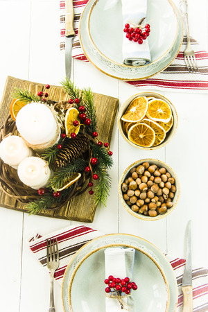 a table setting for Christmas with a viburnum on a plate and an ornament from a Christmas wreath with candlesの写真素材