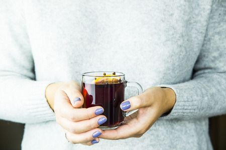a girl in a gray sweater is holding a cup of hot mulled wine with an orange sliceの写真素材