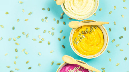 bright appetizers in the form of sauces on a blue background among pumpkin seeds. Hummus, carrot and...