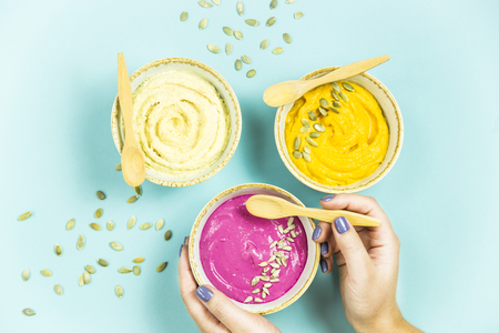 a woman holds a beetroot sauce next to bright snacks - hummus of chickpeas and carrot sauce among pumpkin seeds. Top view. Flat layの写真素材