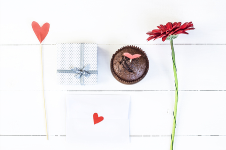 St. Valentine's Day concept. Holiday decoration. A gift, a red flower, a paper heart on a stick, a chocolate muffin and a love letterの写真素材