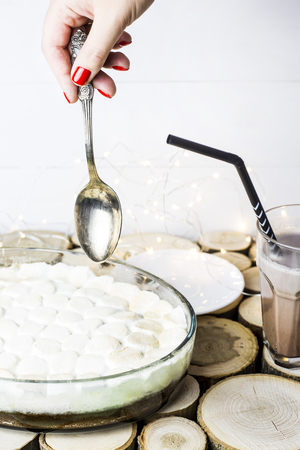 A woman takes a serving of chocolate cake with baked marshmallow - a winter dessert next to a cup of cocoaの写真素材