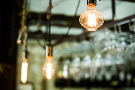 Decorative light bulbs with yellow light hang over the bar in front of the glasses