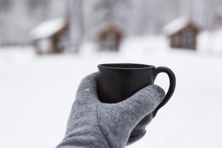 A female hand in a glove holds a cup of coffee in a snowy forestの写真素材