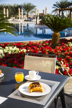 Breakfast of croissants with chocolate pasta and orange juice and coffee at the table on the terrace by the poolの写真素材