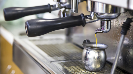 make espresso with a coffee machine. Fresh coffee goes from machine to metal jugの写真素材
