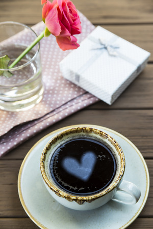 The heart is reflected in a cup of coffee on the table next to the rose. Valentine's Day Conceptの写真素材