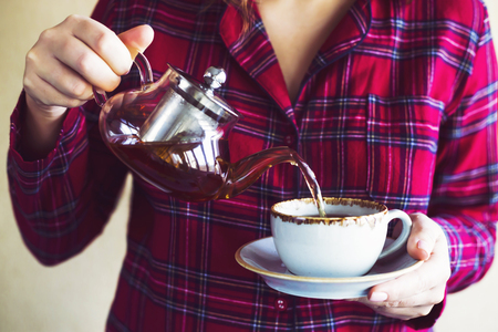 A girl in red checkered pajamas pours morning teaの写真素材