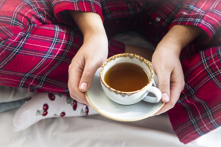 A girl sitting in pajamas from the bed holds a cup of hot tea. Morning home conceptの写真素材