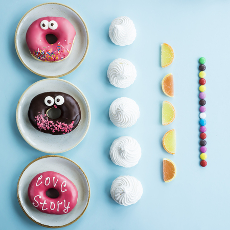 Unhealthy sweet food laid out in even rows on a blue background - donuts, meringue, marmalade, chocolate stick. Minimalism. Junk food conceptの写真素材