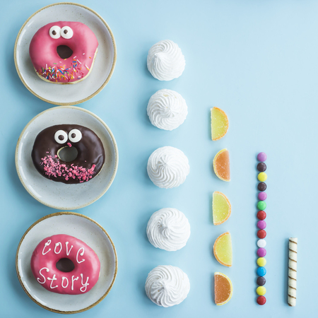 Unhealthy sweet food laid out in even rows on a blue background - donuts, meringue, marmalade, chocolate stick. Minimalism. Junk food conceptの写真素材