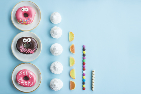 Unhealthy sweet food laid out in even rows on a blue background - donuts, meringue, marmalade, chocolate stick. Minimalism. Junk food conceptの写真素材