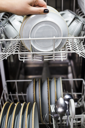 A woman's hand takes a clean saucer out of the dishwasher. Home equipment for cleaning. Work at home conceptの写真素材
