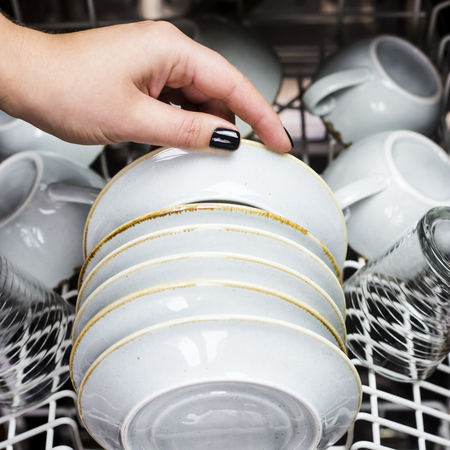 A woman's hand takes a clean saucer out of the dishwasher. Home equipment for cleaning. Work at home conceptの写真素材