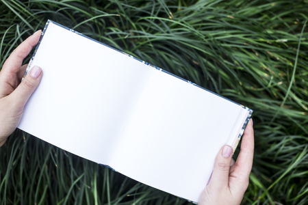 Mock-up of rectangle notepad that the woman is holding in the hands on a background of green grass. Nature and business, study conceptの写真素材