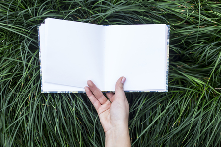 Mock-up of rectangle notepad that the woman is holding in the hands on a background of green grass. Nature and business, study conceptの写真素材