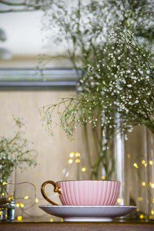 Pink vintage cup with tea on the cupboard near the mirror among the white dry flowers gypsophila. Home interior and still lifeの写真素材
