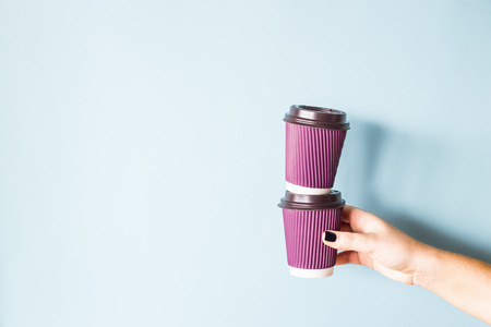 Purple paper kraft disposable cups for coffee with plastic lids in a female hand. One glass stands on the other. Tower of coffee. On blue backgroundの写真素材