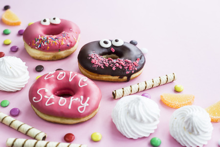 Junk food. Donuts, marmalade, chocolate sticks and balls, and meringues are scattered on a pink background. Unhealthy food conceptの写真素材