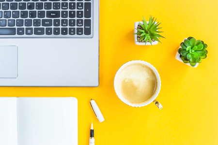 Workplace with a laptop, bklonotom, pen, a cup of coffee and green whiskers in white pots. The working space of a  Top view. Flat layfreelancer, journalist, writer, modern worker. On a bright yellow background.の写真素材