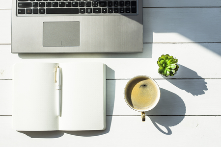 Workplace with laptop and notepad next to a cup of coffee. On a white table next to the house plants are succulents. Top view, flat layの写真素材
