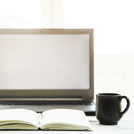 Workplace at the laptop monitor with a notebook on a white table. Minimalistic design. Sunlight - easy tintingの写真素材