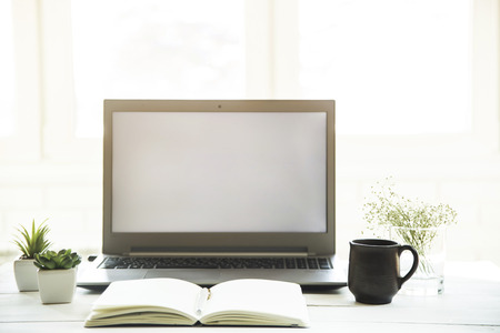 Workplace at the laptop monitor with a notebook on a white table. Minimalistic design. Sunlight - easy tintingの写真素材