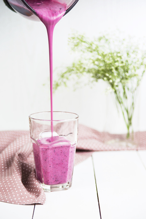 Banana currant smoothies are poured into a glass on a white table next to a pink napkin in polka dots. Against the background of delicate white and green colorsの写真素材