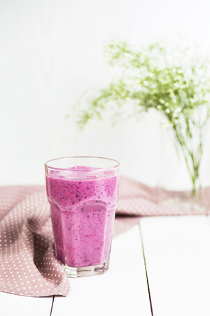 Banana currant smoothies in a glass on a white table next to a pink napkin in speckles. Against the background of delicate white and green colorsの写真素材