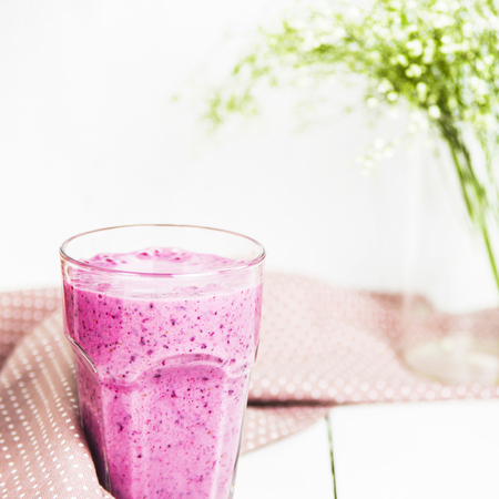 Banana currant smoothies in a glass on a white table next to a pink napkin in speckles. Against the background of delicate white and green colorsの写真素材