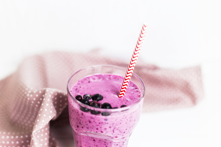 Banana currant smoothies in a glass on a white table next to a pink napkin in speckles with a straw. With black currant berries on the surfaceの写真素材