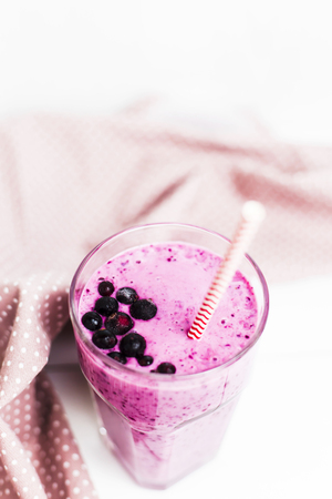 Banana currant smoothies in a glass on a white table next to a pink napkin in speckles with a straw. With black currant berries on the surfaceの写真素材