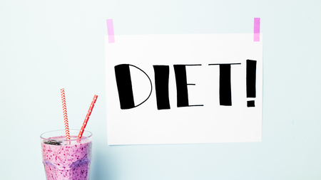 Banana currant smoothies of violet color with red straws on a blue background with a sign "Diet", which is attached with pink tapeの写真素材