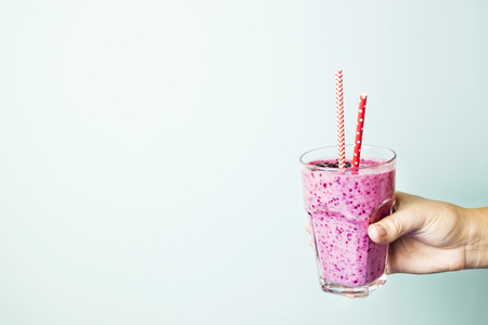 Banana currant smoothies of violet color with red straws on a blue background in the hand. Healthy food and diet concept . Background, copyspaceの写真素材